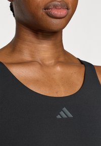 Μαύρο αθλητικό τοπ με ομαλή υφή, διαθέτει χαμηλή λαιμόκοψη σε σχήμα scoop και μικρό γκρι λογότυπο Adidas στο στήθος.