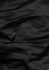 Tissu en denim noir avec une texture de tissage diagonal visible et de doux plis créant des ombres et des reflets subtils.