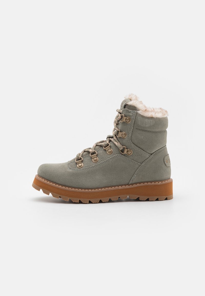 Botte d'hiver en suède gris avec doublure en fourrure, lacets à l'avant, œillets métalliques, et semelle en caoutchouc marron avec des crampons profonds pour une meilleure adhérence.