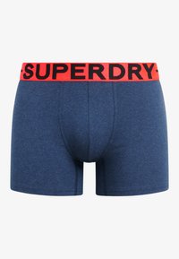 Blauwe boxershorts van zacht materiaal met een aansluitende pasvorm. Voorzien van een brede rode tailleband met zwart "SUPERDRY"-merken.