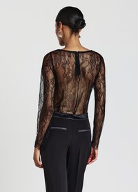 Top in pizzo nero con maniche lunghe, caratterizzato da un retro trasparente e colletto rotondo. Abbinato a pantaloni neri a vita alta rifiniti con satin.
