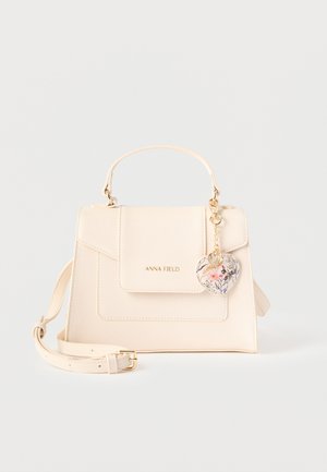 Μικρή κρεμ τσάντα χειρός με πάνω λαβή, ρυθμιζόμενο ιμάντα ώμου, εμπρόσθιο καπάκι με το λογότυπο «ANNA FIELD» και φλοράλ μπρελόκ σε σχήμα καρδιάς.