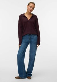Maglione bordeaux con scollatura a V e colletto, abbinato a jeans di denim blu a zampa d'elefante. Tessuto morbido, vestibilità rilassata e design monocromatico.
