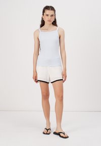 Lyseblå ribbet tanktop med firkantet utringning, parret med hvite shorts med polkadotter og svart blondekant; modellen har svarte flip-flops på.