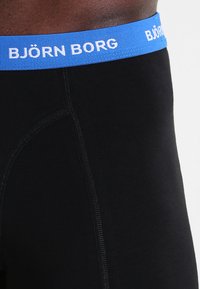 Boxeri negri din material elastic cu un brâu albastru, având branding alb "BJÖRN BORG". Materialul pare neted și mulat.