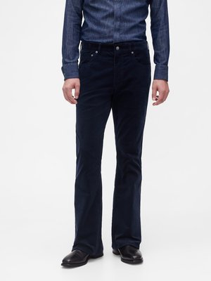 Pantalon en velours côtelé bleu foncé, coupe droite, cinq poches, et détails en métal. Porté avec une chemise en jean boutonnée.