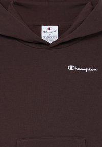 Brun hettegenser med frontlomme, med en hvit brodert "Champion"-logo på brystet og en standard størrelse-lapp inni kragen.