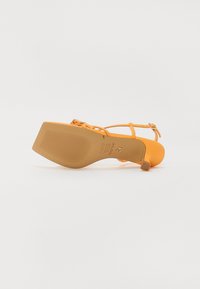 Sandale à talon orange avec des fines brides et une semelle texturée. Dotée d'un bout carré et d'une bride de cheville ajustable pour un maintien sécurisé.