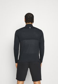 Svart långärmad atletisk tröja med hög krage, med ett strukturerat meshpanel över ryggen och minimalistiska loggoprints. Kombineras med svarta shorts.