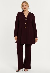 Bordeaux pak met een lange blazer met vijf gouden knopen, nauwsluitende pasvorm en uitlopende broek, gemaakt van gladde stof met een lichte glans.