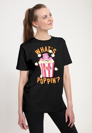 Sort t-shirt med grafisk tryk af en pink bjørn i en popcornboks, med teksten "HVAD SKEJER?" i klare farver. 100% bomuldsmateriale, kortærmet.