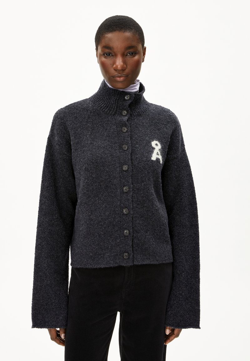 Cardigan tricoté gris foncé avec un col haut, une fermeture à boutons et des manches surdimensionnées. Présente un logo brodé blanc sur la poitrine.