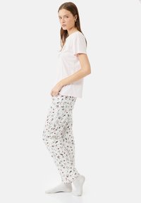Camiseta de manga corta de color rosa claro combinada con pantalones de pijama blancos que presentan coloridos patrones de dibujos animados. La tela parece suave y casual.