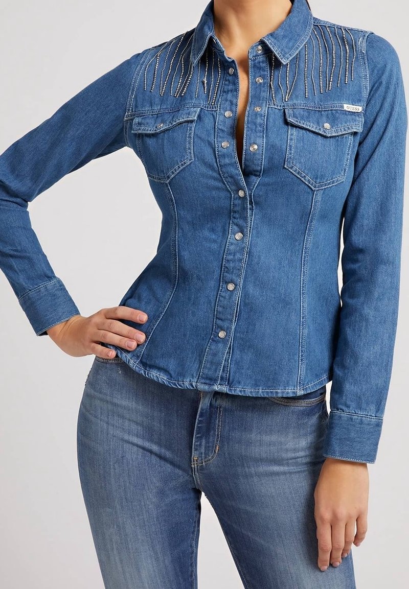 Camicia di jeans blu scuro con maniche lunghe, forma aderente, due tasche sul petto e decorazioni in argento lungo le spalle.