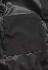 Mustast kangast tasku siledal, mati pinnal; ühtlane tekstuur; ristkülikukujuline puhaste servade ja minimaalse õmblusega.