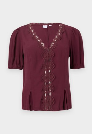 Blouse bordeaux à manches courtes avec bordure en dentelle festonnée le long du col en V et devant boutonné, présentant de légers plis près de l'ourlet.