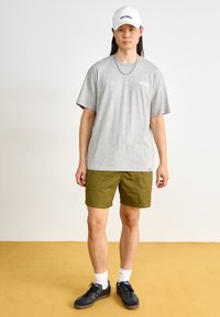 Gray cotton t-shirt with short sleeves, paired with olive green shorts. Black sneakers and white cap with "DICKIES" logo.