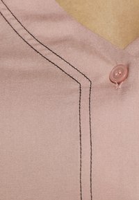Rosa tyg med en jämn yta, med svarta sömmar och en rund rosa knapp på en v-ringad design, som visar en skräddarsydd form.