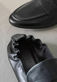 Mustad musta nahast slip-on kingad, millel on sile viimistlus, ümar varvas ja klanitud elastne ääreosa kontsapooles. Sisepealsetel on tekst "SIGNATURE MADE IN BRAZIL."