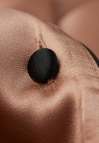 Satin tyg i en mjuk rosa färg med en rund svart knappdetalj. Texturen är slät med synlig sömnad på kanten.