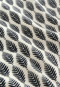 Valge kangas, millel kordub musta sõnajalalehed meenutav muster, esitatuna õrnade voldikutega, mis tekitavad pehmeid varje.