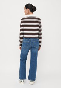 Brun og hvitstripet avkortet langermet skjorte kombinert med blå vide jeans. Modell vist fra bakfra, iført hvite joggesko.