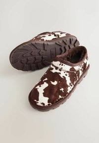 Papuci cu imprimeu de vacă maro și alb, fabricați din blană moale, cu o talpă din cauciuc durabilă și un design rotunjit pentru confort.