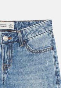 Ανοιχτό μπλε τζιν παντελόνι με χαλαρή εφαρμογή, με εμφανή ραφές, πάνω κουμπί και ετικέτα με ρυθμιζόμενη μέση. Υφή υφάσματος με ανάγλυφη επιφάνεια.