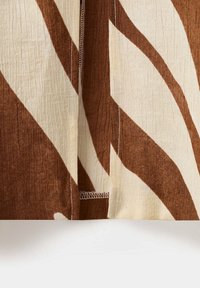 Gros plan d’un tissu marron et crème avec des rayures abstraites audacieuses et des coutures visibles le long du matériau texturé.