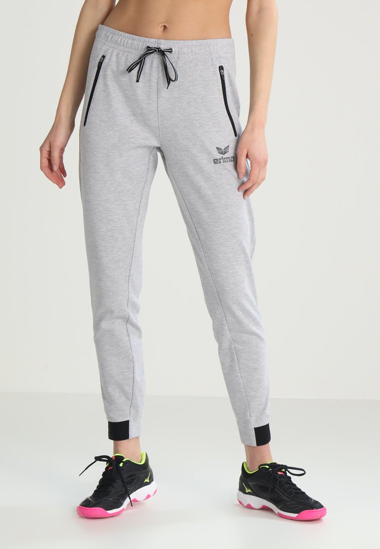 Pantalones de chándal grises hechos de una tela suave, con una cintura elástica, cordón negro, bolsillos laterales con cremallera y puños negros en los tobillos.