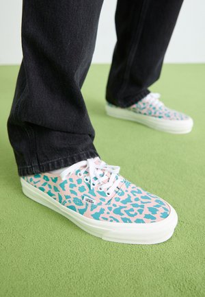 Baskets en toile avec une base rose et un design léopard bleu, lacets blancs et une semelle en caoutchouc blanc, portées avec un pantalon en denim noir.