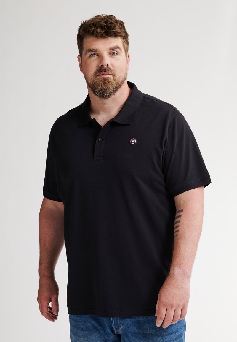 Mustapolo, jossa on kaulus ja lyhyet hihat, vasemmassa rinnassa on pieni pyöreä logo. Materiaali vaikuttaa sileältä ja kevyeltä.