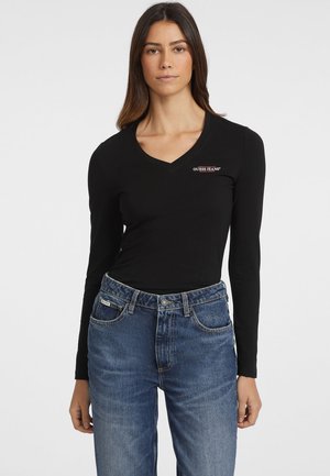 Crna dugorukava majica s V-izrezom i prilagođenim dizajnom. Ima suptilan "Guess Jeans" logo u živopisnoj veznoj tehnici na prednjem dijelu.