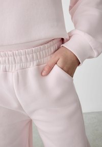 Ljust rosa sweatshirt och matchande byxor med elastisk midja och manschetter; mjukt material; hand i sidofickan.