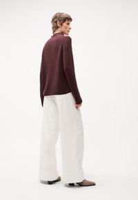 Maglione a maglia borgogna con colletto alto, abbinato a pantaloni bianchi larghi e scarpe con tacco a blocco marroni. Design e texture semplici e moderni.