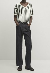 Czarny i biały t-shirt w paski z dekoltem w serek, zestawiony z dżinsami w kolorze ciemnym o wysokim stanie. Sandały mają plecione paski.