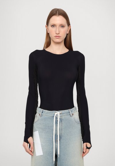 Svart langermet bodysuit med frynser på ermene, parret med lyseblå høytlivsjeans og hvit snøring. Glatt tekstur.