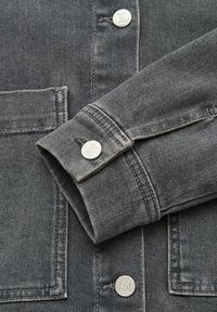 Donkergrijze denim jas mouw over de voorkant gevouwen met zilverkleurige metalen knopen en zichtbare stiksels van het rechthoekige voorvak.