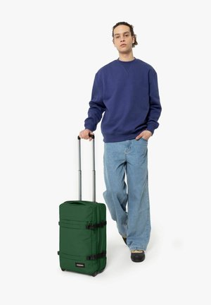 Maleta verde con ruedas, fabricada en tejido duradero, que cuenta con un asa en la parte superior, un asa ajustable y hebillas negras para asegurar el contenido.