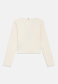 Kremi spalvos ilgomis rankovėmis trumpa palaidinė su raukšlėtu raštu, V formos iškirpte ir lygiais siūlėmis. Paprastas dizainas be raštų ar matomų detalių.