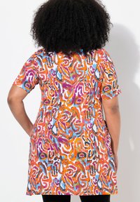 Kolorowa tunika z abstrakcyjnym wzorem w odcieniach pomarańczowego, niebieskiego i fioletowego. Krótkie rękawy i luźny krój, wykonana z lekkiego materiału.