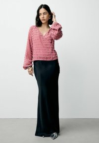 Rosa, struktureret langærmet top med V-udskæring, parret med en slank sort, gulvlængde nederdel. Sølvfarvede spidse sko fuldender outfittet.