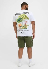 Camiseta blanca con un colorido diseño botánico en la parte trasera, combinada con pantalones cortos cargo de color verde oliva y zapatillas blancas.
