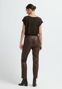 Bruine faux leren broek met een hoge taille, gecombineerd met een losvallend, donkerbruin bovenstuk. Eenvoudig ontwerp, gladde textuur en rechte pijpen.