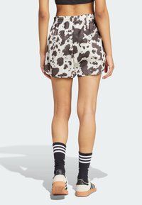 Kratasy s potiskem kravské srsti v černobílé barvě, s elastickým pasem, hladkým materiálem a bočními rozparky pro snadný pohyb, zkombinované s pruhovanými ponožkami a teniskami.