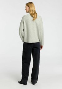 Světle šedý pletený svetr s volným střihem, spadlými rameny a žebrovaným lemem, v kombinaci s tmavomodrými džínami s vysokým pasem.