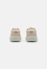 Sneaker giallo e beige con tomaia in suede testurizzato, accenti in pelle bianca e suola in gomma rigata. Design minimalista senza branding visibile.