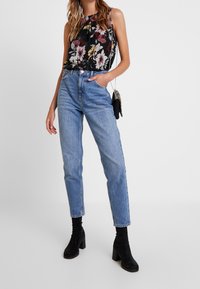 Floral sleeveless top with a black background, paired with high-waisted light blue denim jeans and black heeled ankle boots.