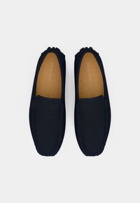 Par navy plavih sued loafers s bež ulošcima označenim "Pier One," snimljeni odozgo na bijeloj pozadini.