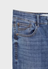 Jeans de mezclilla oscura con un lavado azul desgastado, que presentan remaches de cobre, cinco bolsillos y costuras en contraste. La textura es suave y lisa.